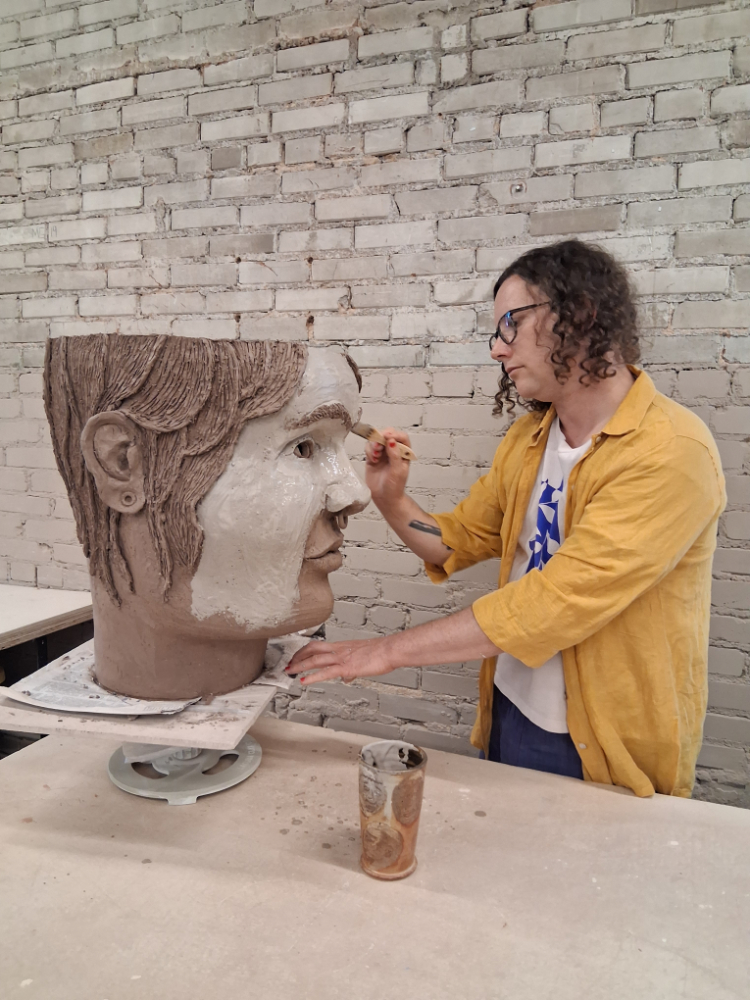 Dylan Cale Jones painting clay slip on a large clay sculpture of a head. 